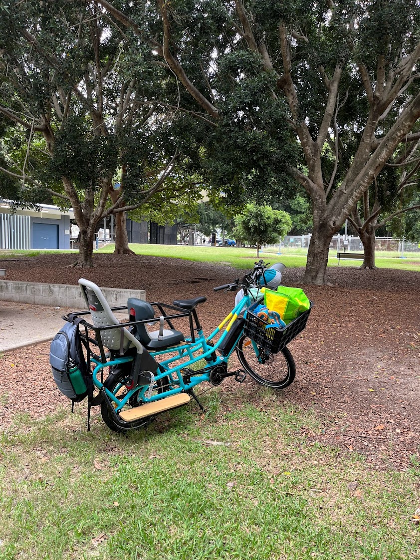 The tribe evamos in a leafy green park. A backpack is attached to the rear of the crew cab. The basket is full of gear.